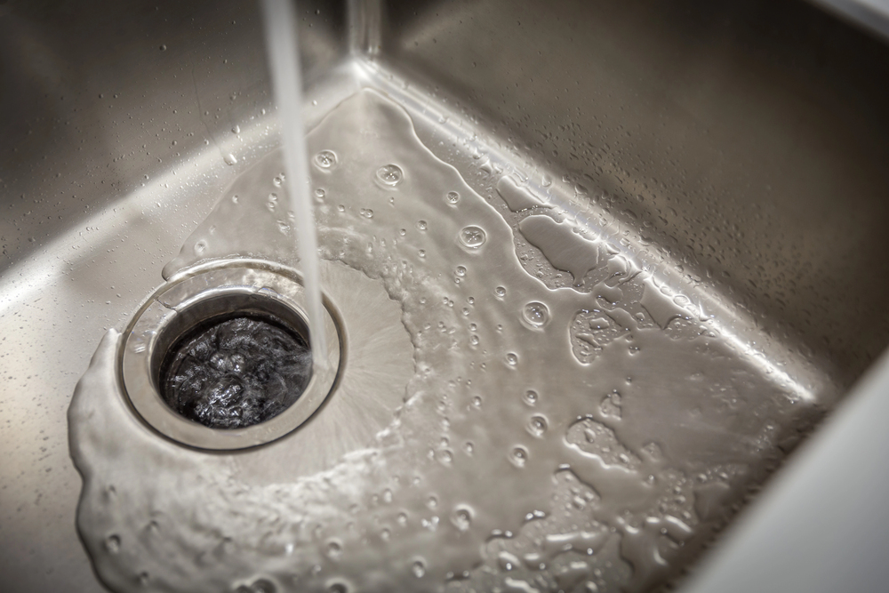 Water is running from a faucet into a stainless steel sink with a garbage disposal installation and repair recently completed, flowing smoothly toward the drain.
